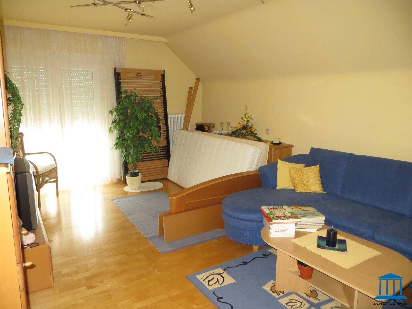 Helles Schlafzimmer mit Parkettboden, blauem Sofa und Dachschräge.