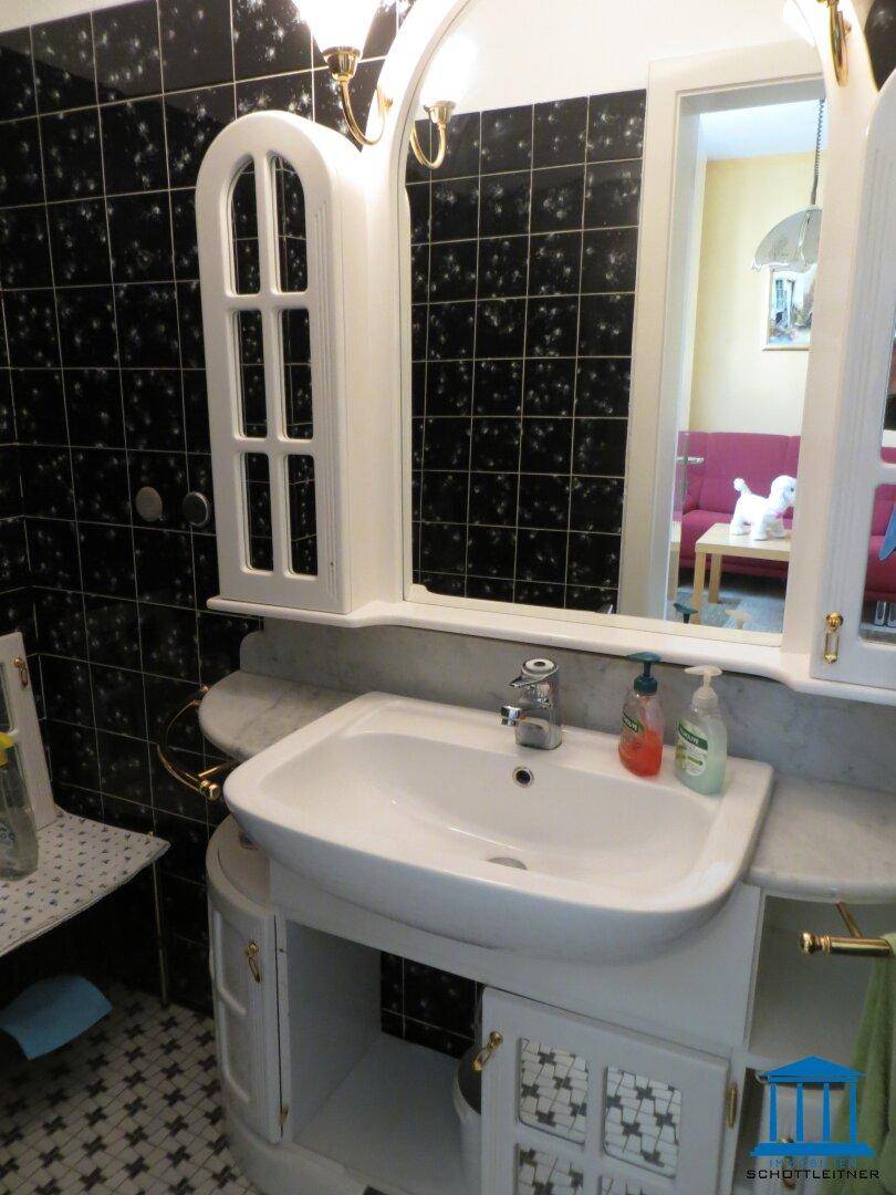 Badezimmer mit schwarzem Fliesenmuster, weißem Waschbecken und Spiegelschrank.