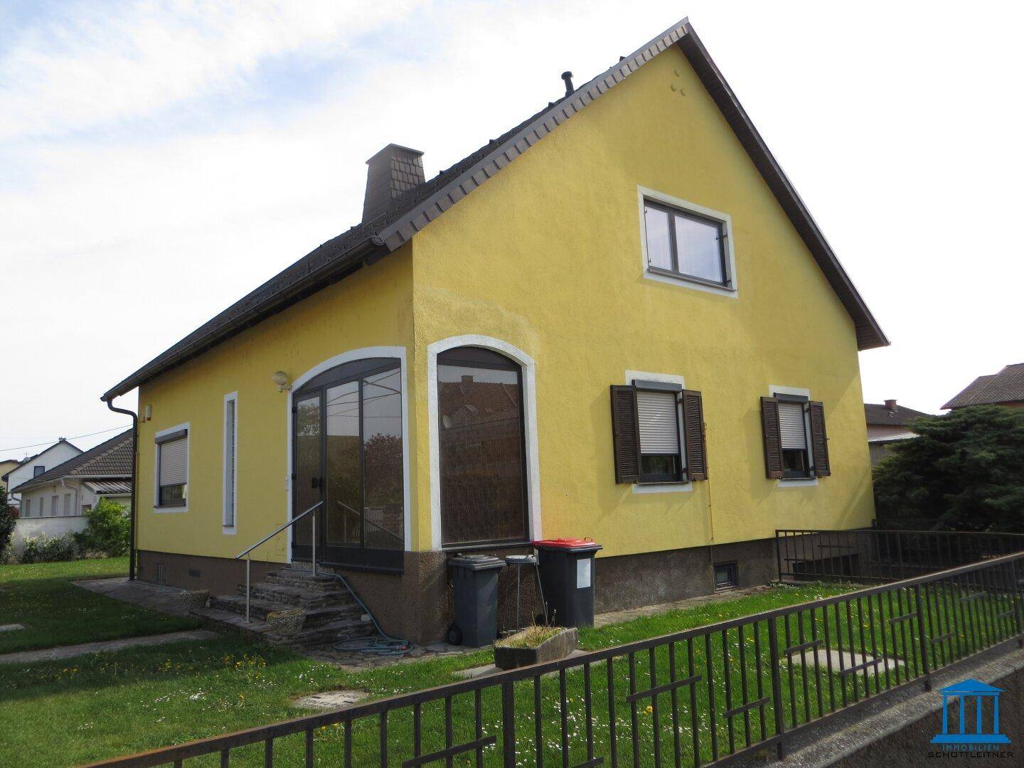 Gelbes Einfamilienhaus mit großen Fenstern und schwarzem Dach.