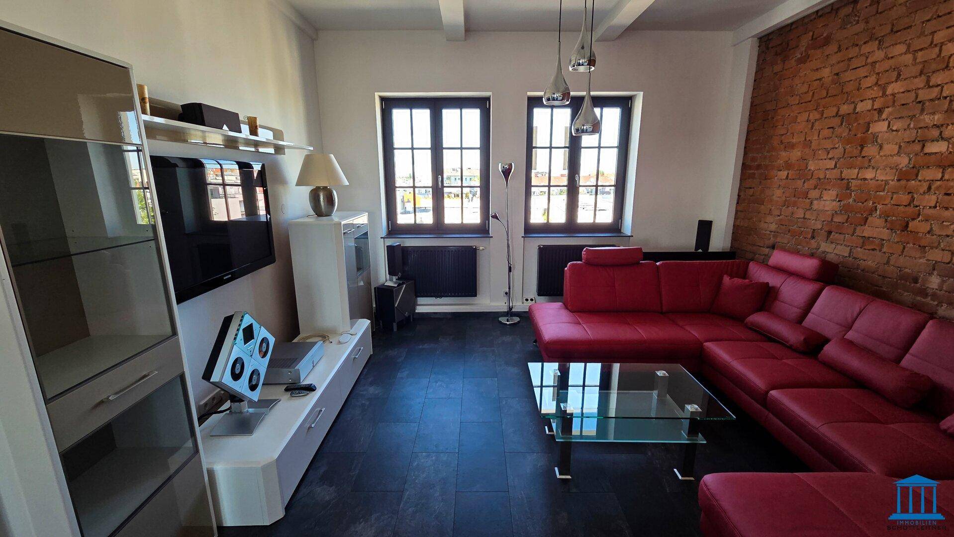 Wohnzimmer mit rotem Sofa, freiliegender Ziegelwand und großen Fenstern.