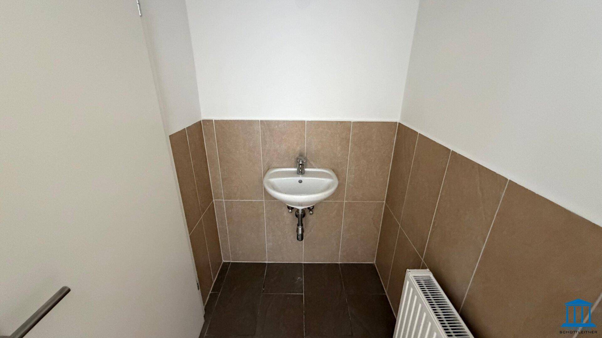 Kleines Gäste-WC mit Waschbecken und braunen Fliesen an der unteren Wandhälfte.