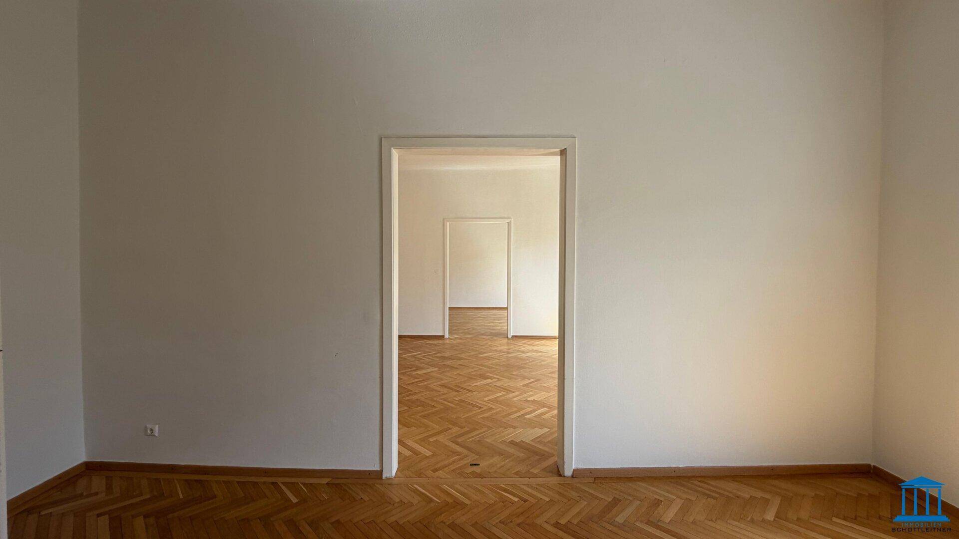 Langer Blick durch offene Türen in mehrere aufeinanderfolgende Zimmer mit Fischgrätparkett.