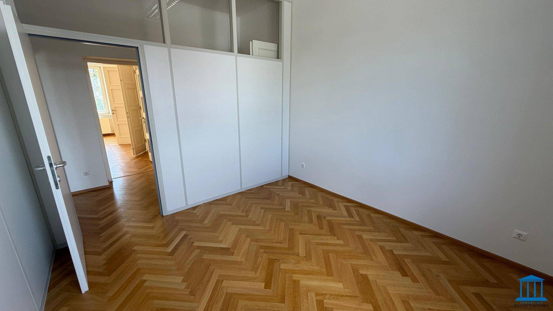 Leeres Büro mit Fischgrätparkettboden und modernen Trennwänden mit oberen Glaspaneelen.