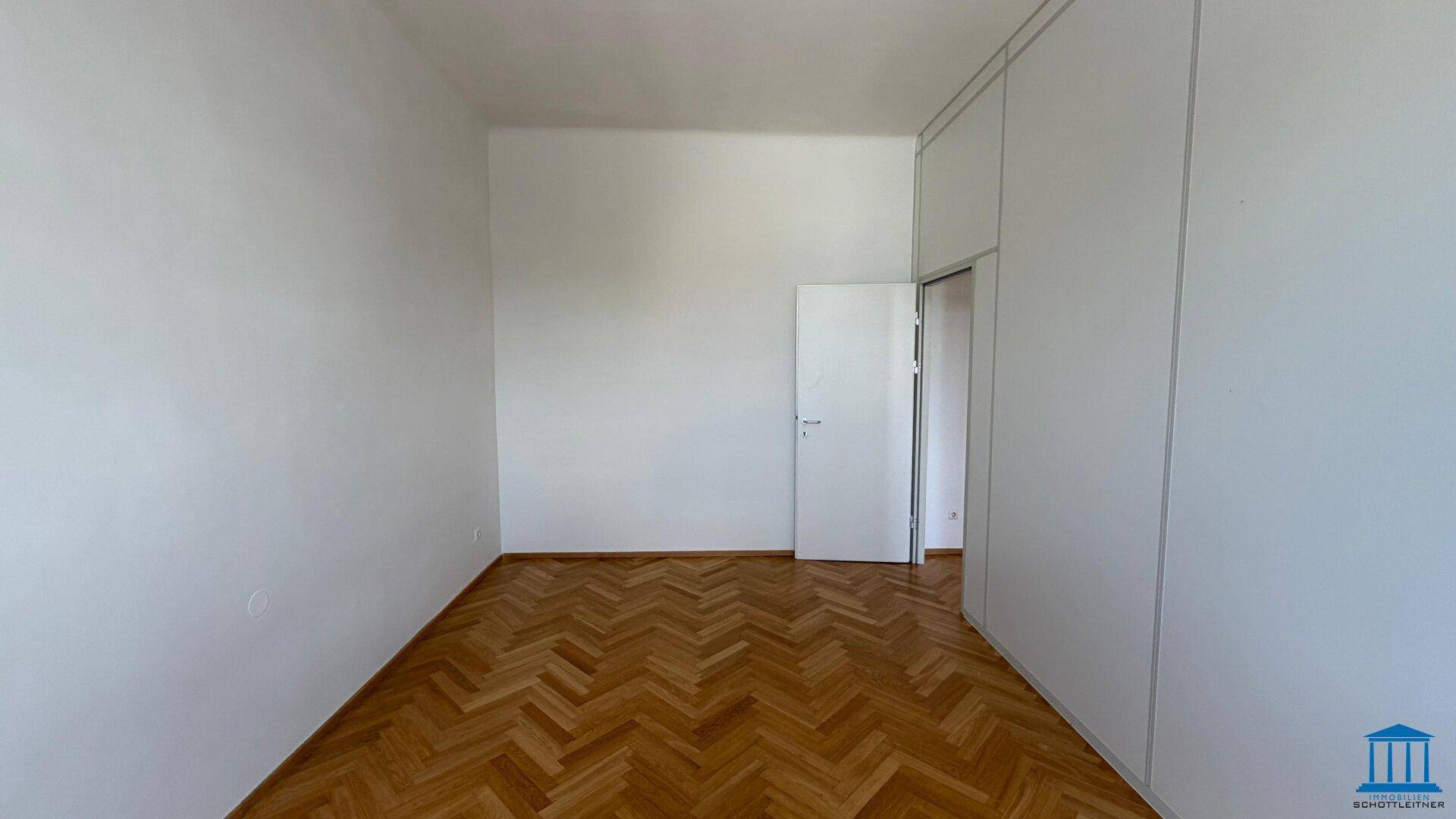 Leeres Büro mit Fischgrätparkettboden, einer Tür und weißen Trennwänden.