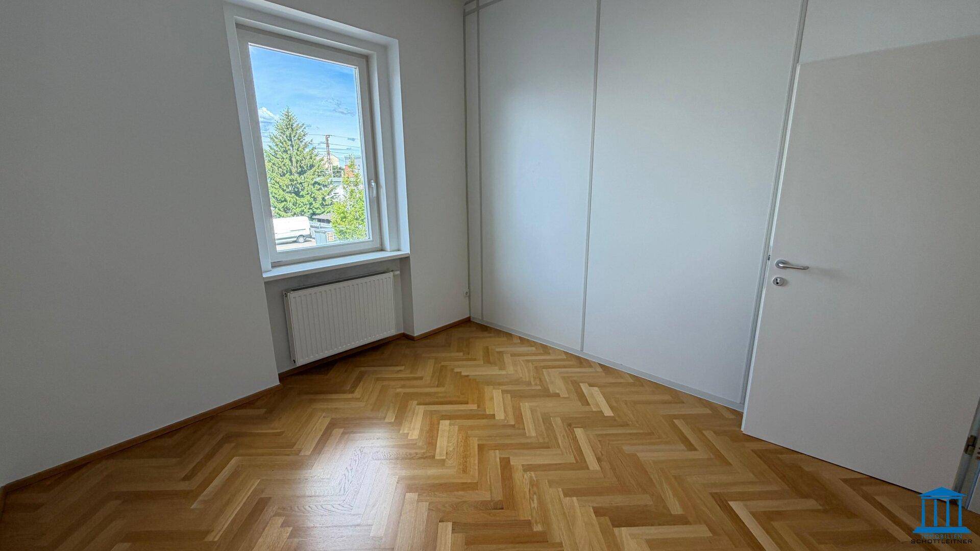 Helles Büro mit Fischgrätparkett, einem Fenster mit Grünblick und Trennwänden.