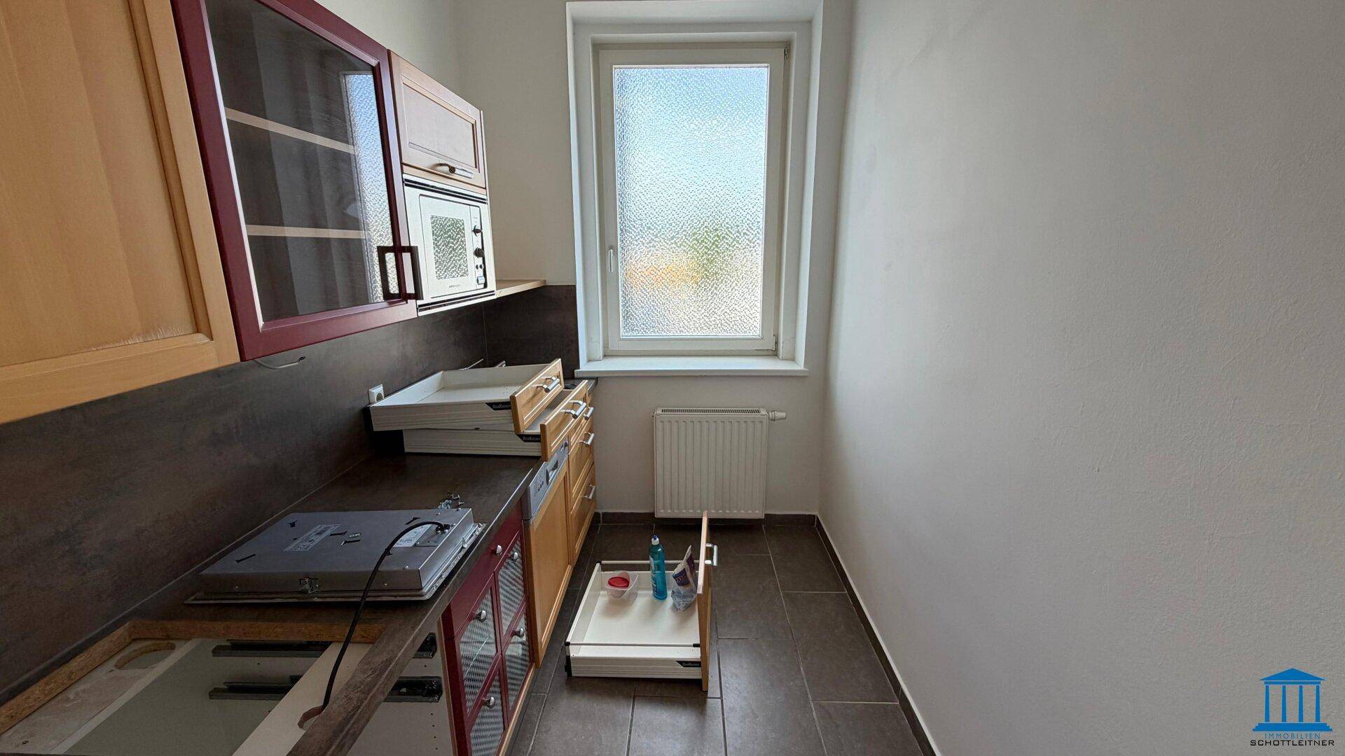 Kleine Küche mit Holzschränken, dunkler Arbeitsplatte, Spülbereich und einem Fenster.