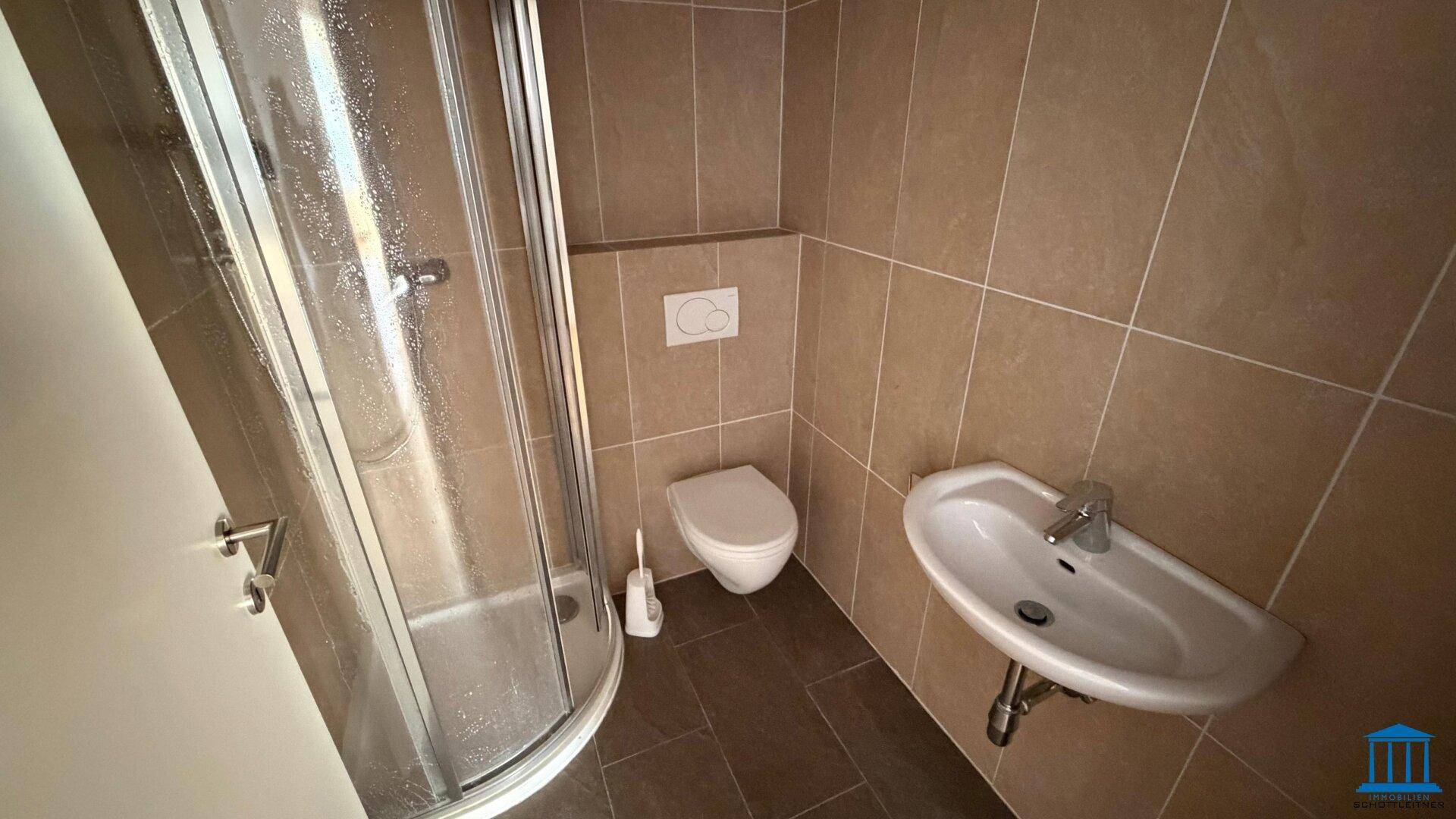 Modernes Badezimmer mit braunen Fliesen, einer Duschkabine, wandhängendem WC und Waschbecken.