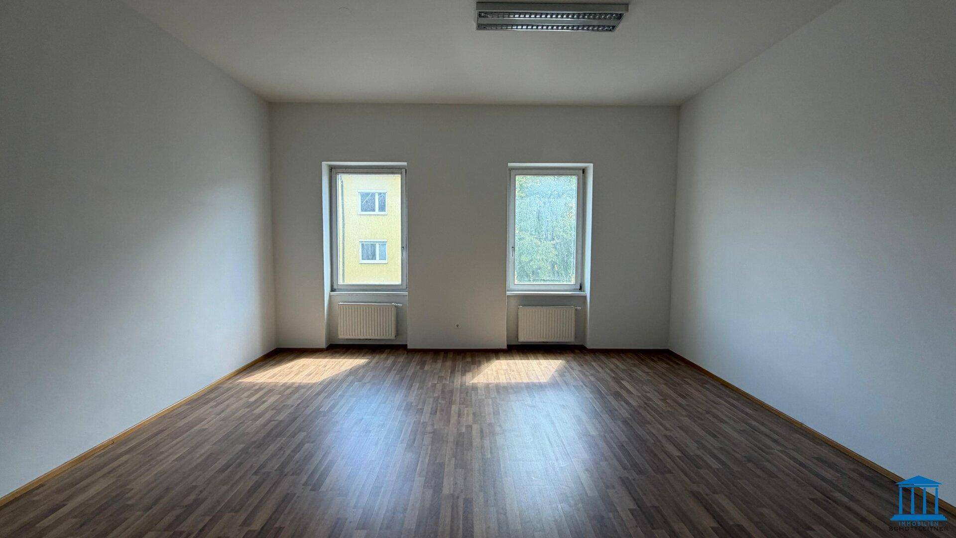 Freundlicher Raum mit zwei Fenstern, die viel Tageslicht hereinlassen, und einem gepflegten Laminatboden.