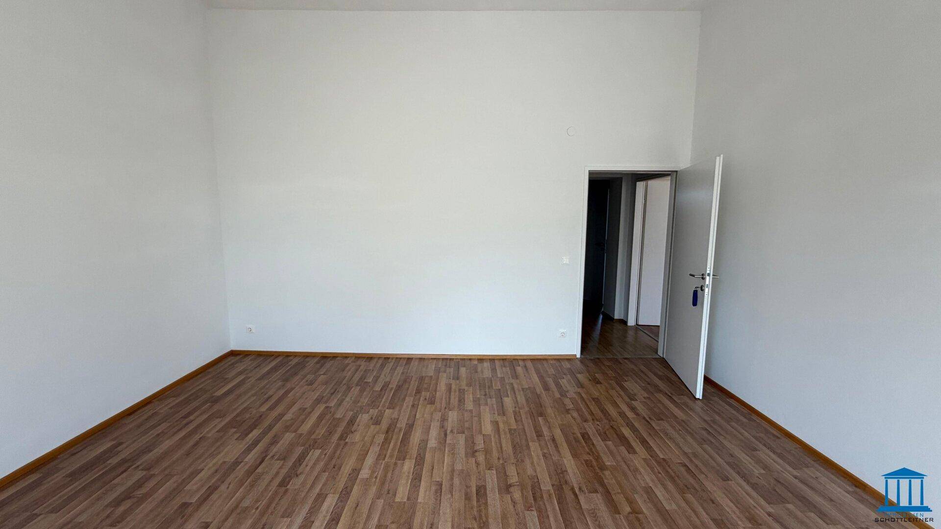 Großer, leerer Raum mit Laminatboden und weiß gestrichenen Wänden, bereit für neue Mieter.