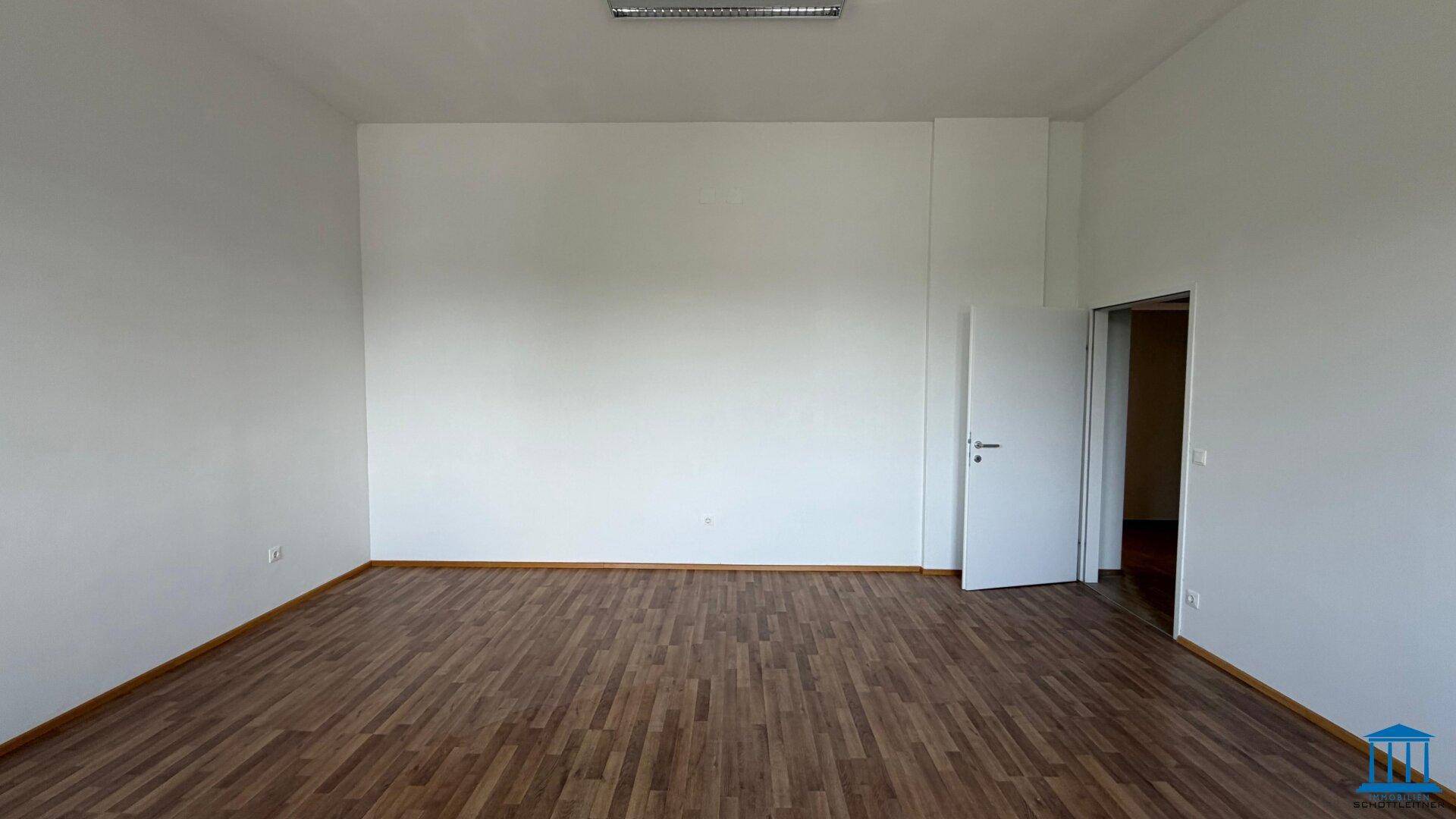 Geräumiger, leerer Raum mit Laminatboden und weiß gestrichenen Wänden, ideal für verschiedene Nutzungen.
