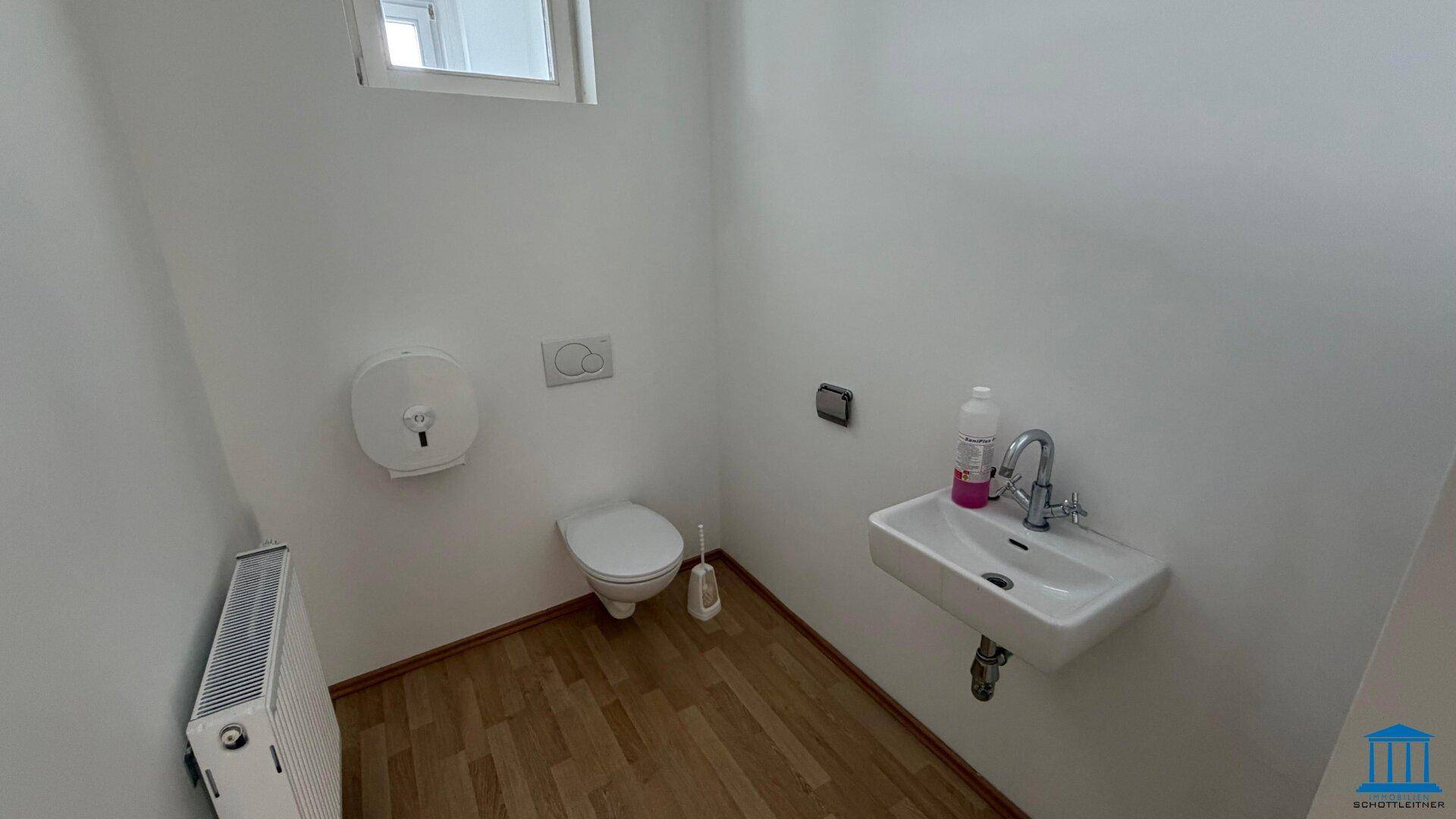 Funktionale Gästetoilette mit WC, Waschbecken, Fenster und Heizkörper, in gutem Zustand.