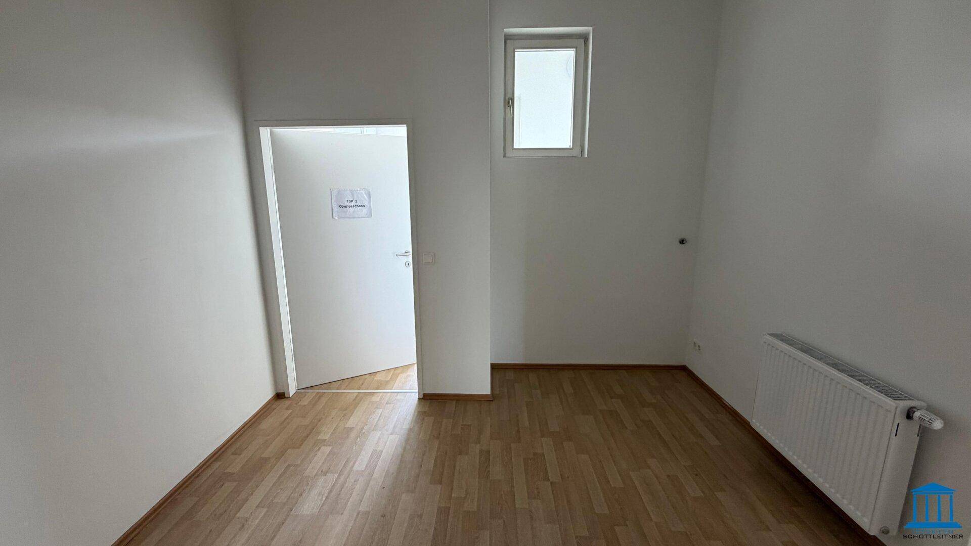 Leerer Raum mit Laminatboden, einem Fenster und Heizkörper, bietet vielseitige Nutzungsmöglichkeiten.