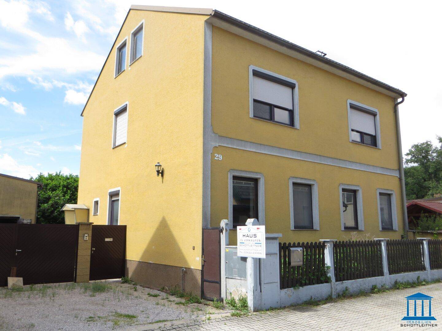 Gelbe Fassade eines Einfamilienhauses mit Rollläden, Vorgartenbereich und Hausnummer 29.