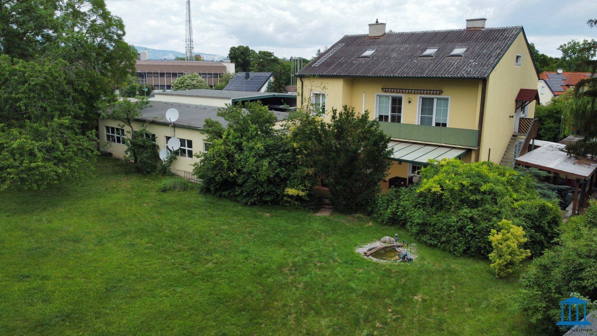 Rückseite des Hauses mit einem großen grünen Garten, einer überdachten Terrasse und einem kleinen Teich.