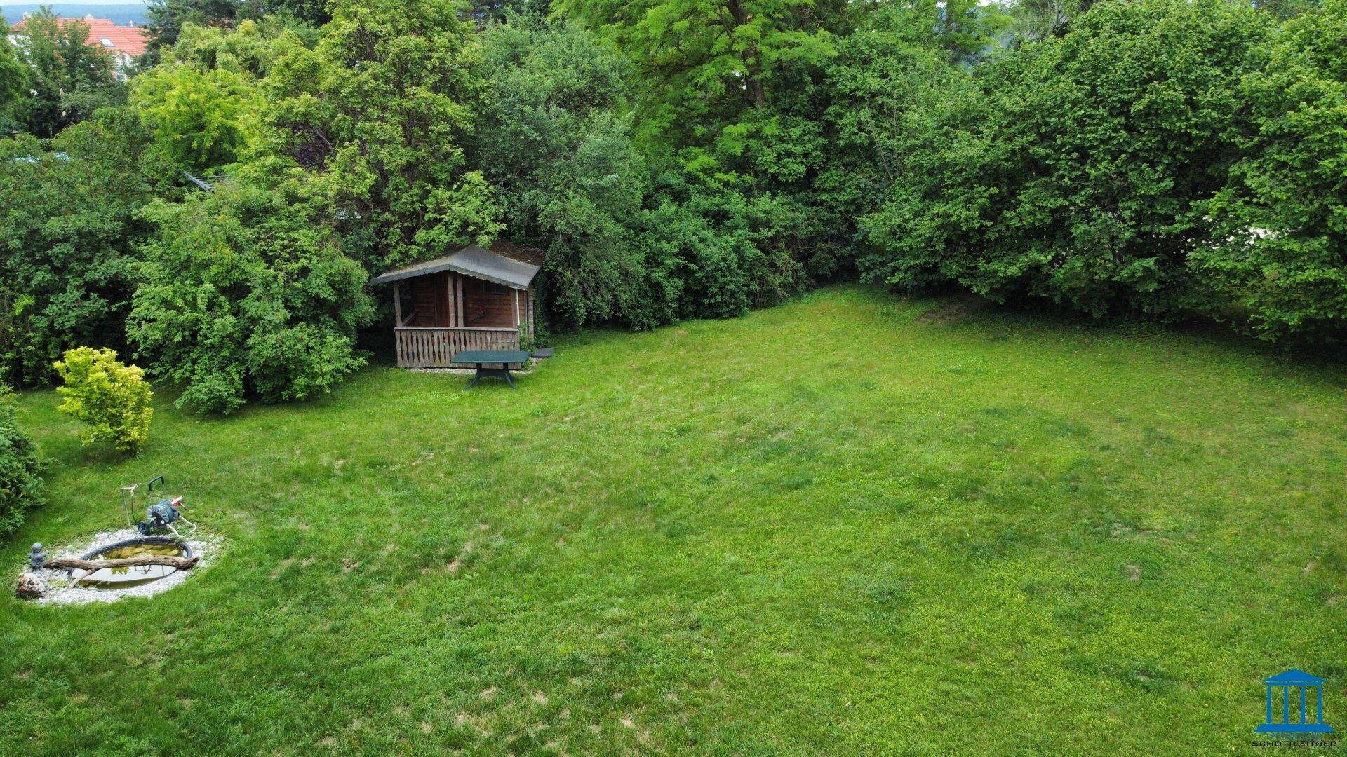 Detailansicht des Gartens mit einem kleinen Holzhaus, einer Bank und einem Teich mit Steinen.