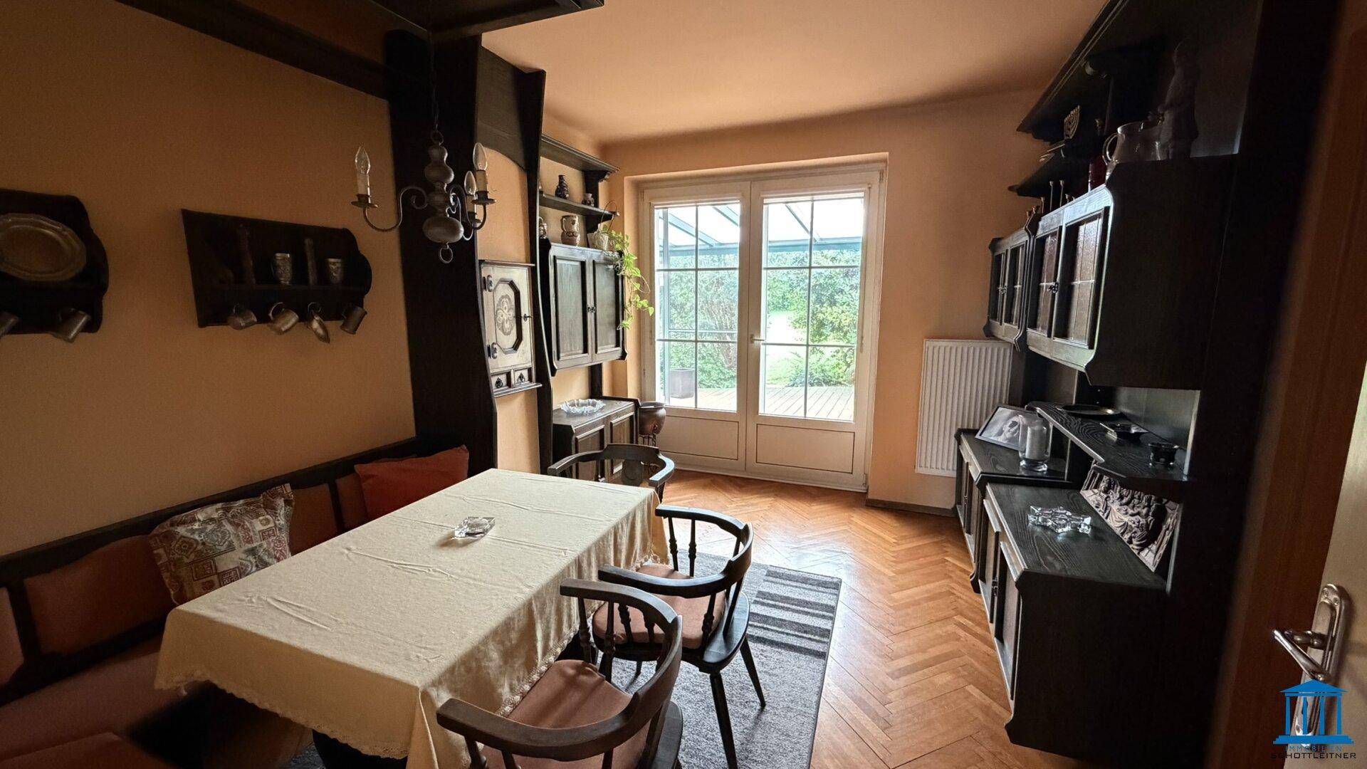 Rustikaler Essbereich mit Holztisch, Sitzbank und Zugang zur Terrasse durch eine Glastür.