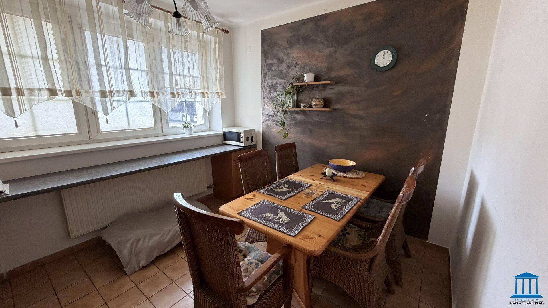 Esszimmer mit Holztisch, Korbstühlen und einer dunklen Akzentwand mit Regalen.