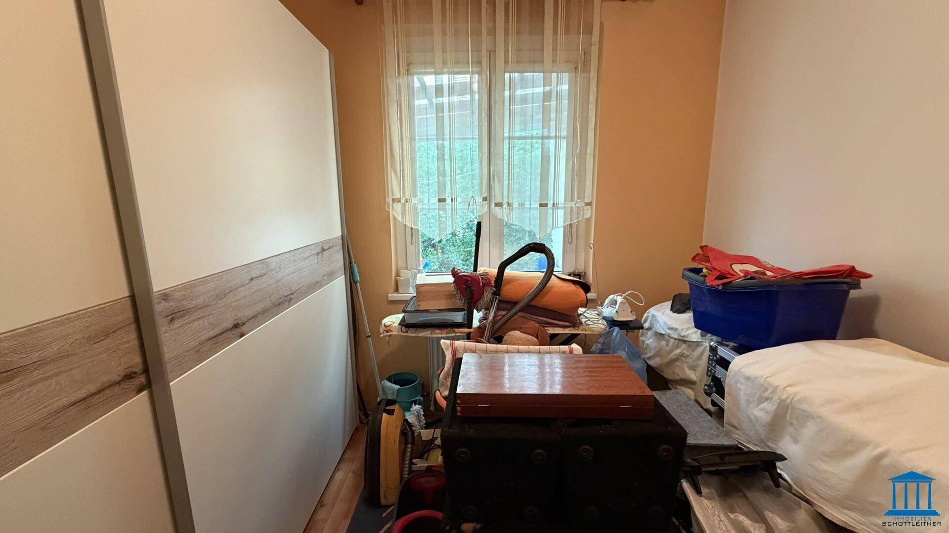 Kleines Schlafzimmer oder Abstellraum mit Fenster, Schrank und verschiedenen Gegenständen.