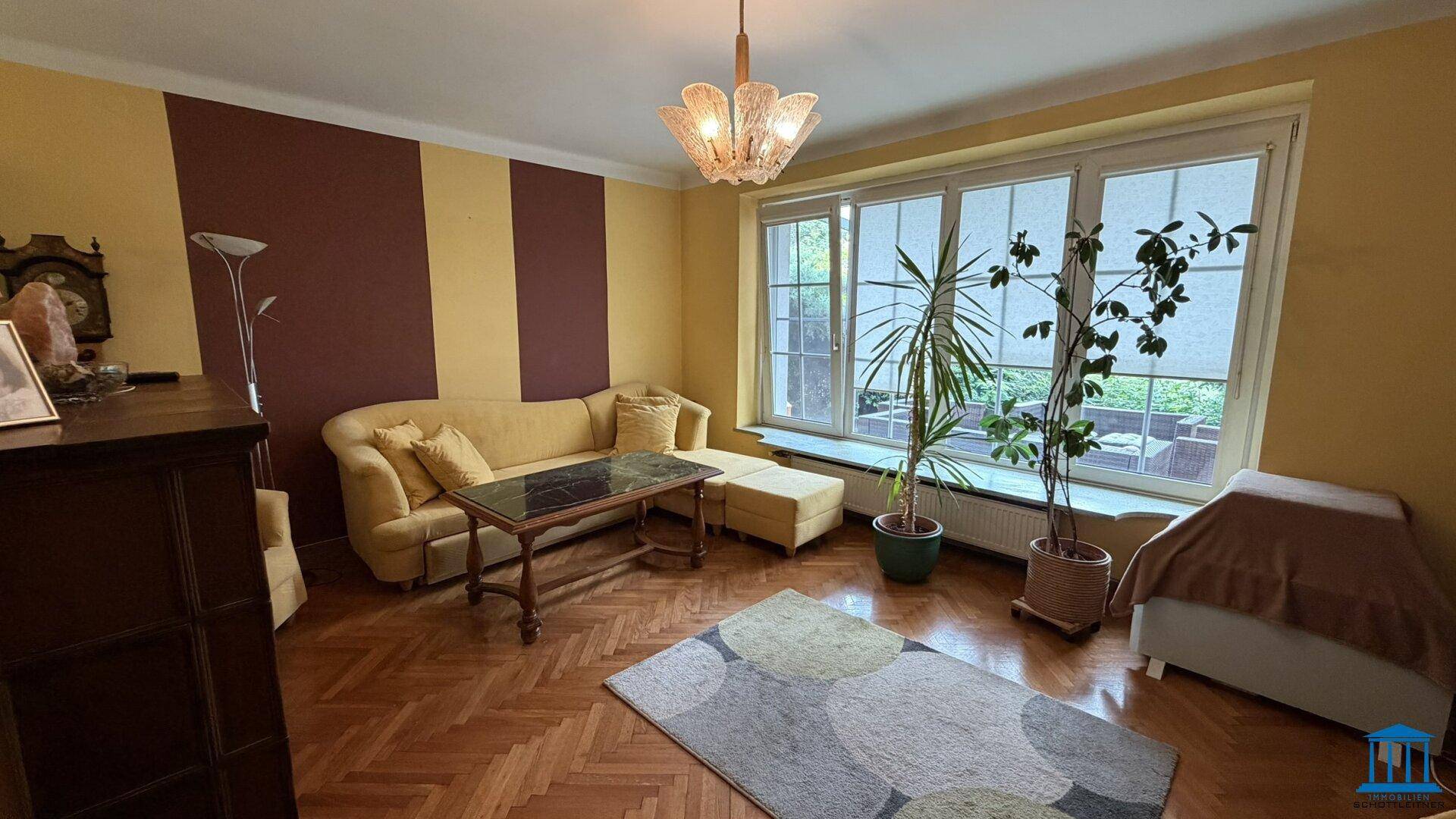 Gemütliches Wohnzimmer mit Parkettboden, gelben Wänden und großem Fenster mit Blick ins Grüne.