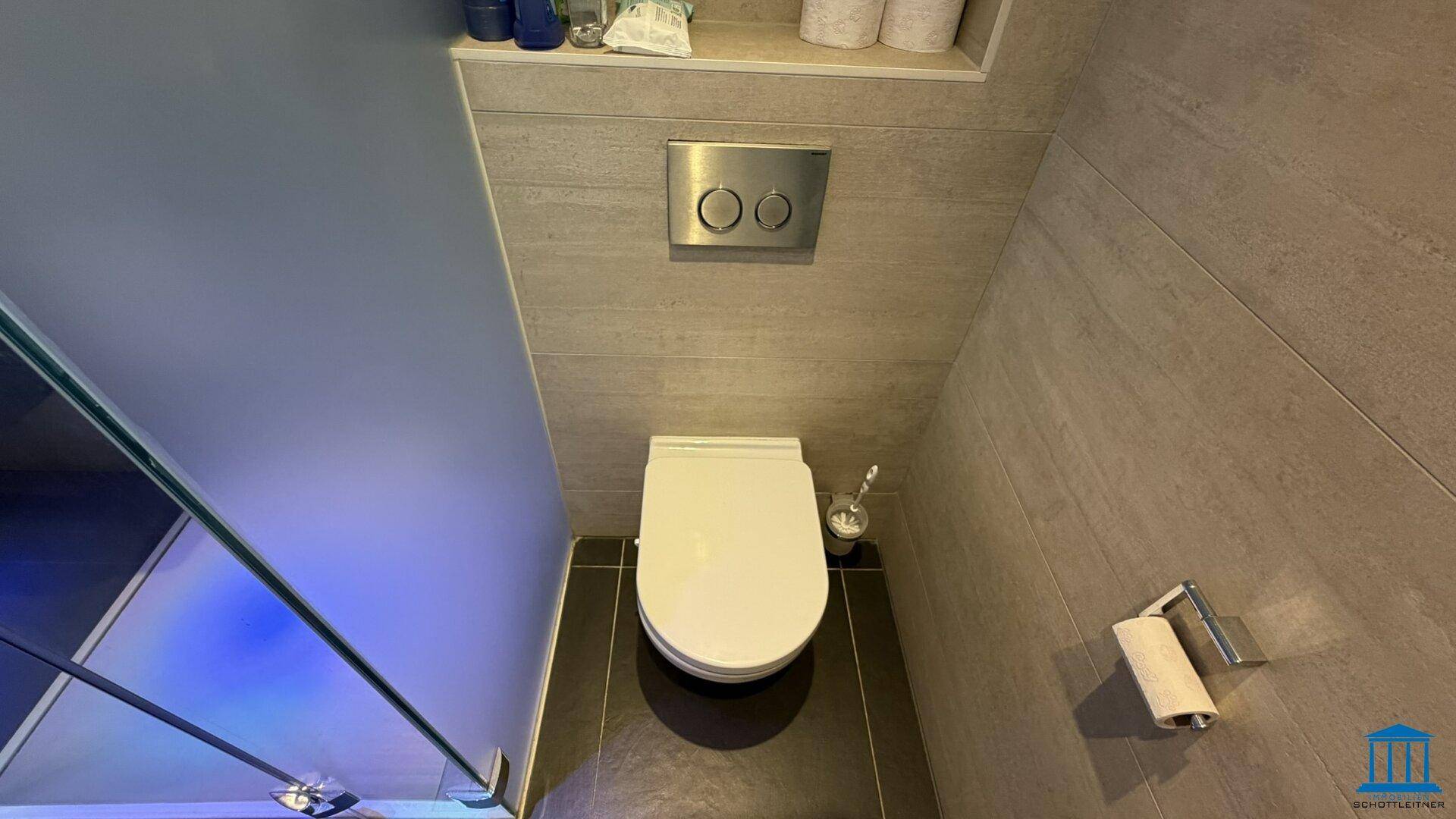 Separate Toilette mit Wand-WC und moderner Spülung in einem gefliesten Raum.