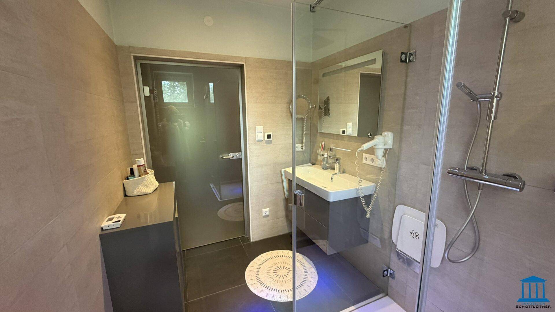 Modernes Badezimmer mit Waschtisch, Spiegel und ebenerdiger Dusche mit Glaswand.