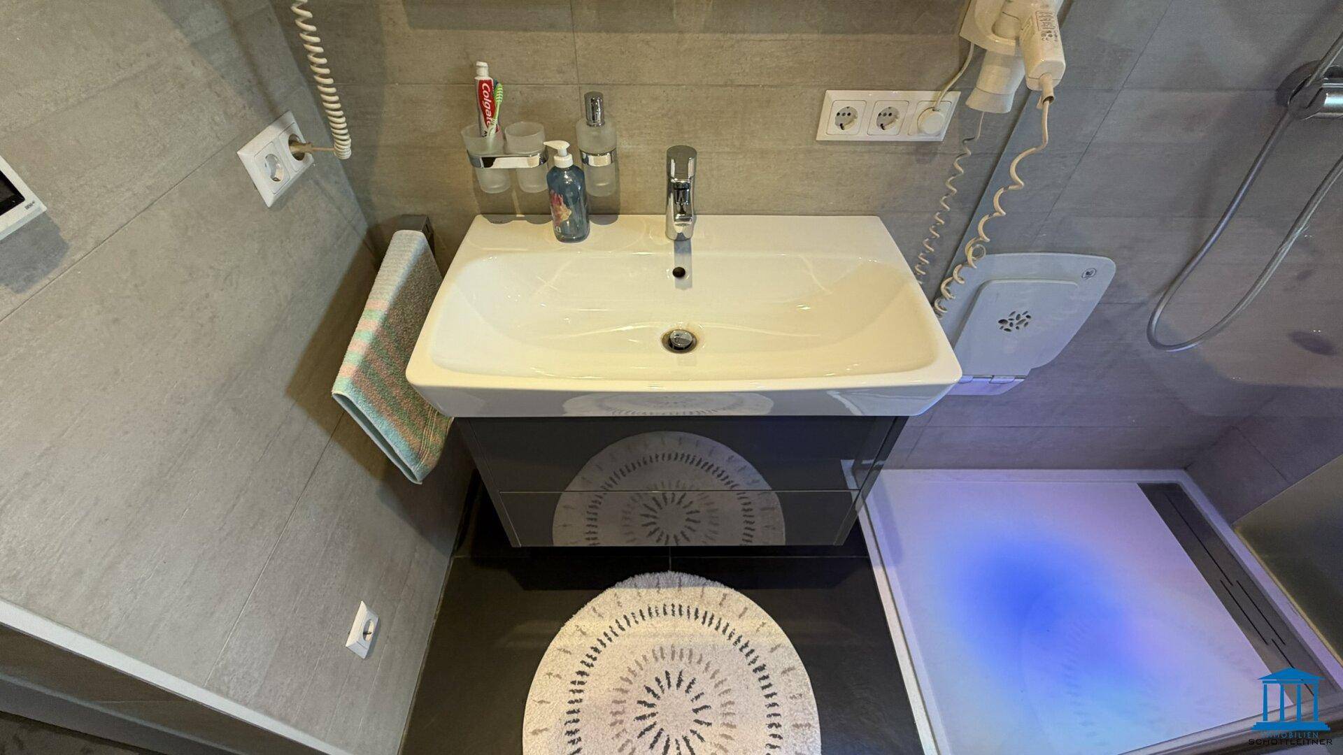 Waschtisch mit modernem Design, Armatur und Spiegel in einem gefliesten Badezimmer.