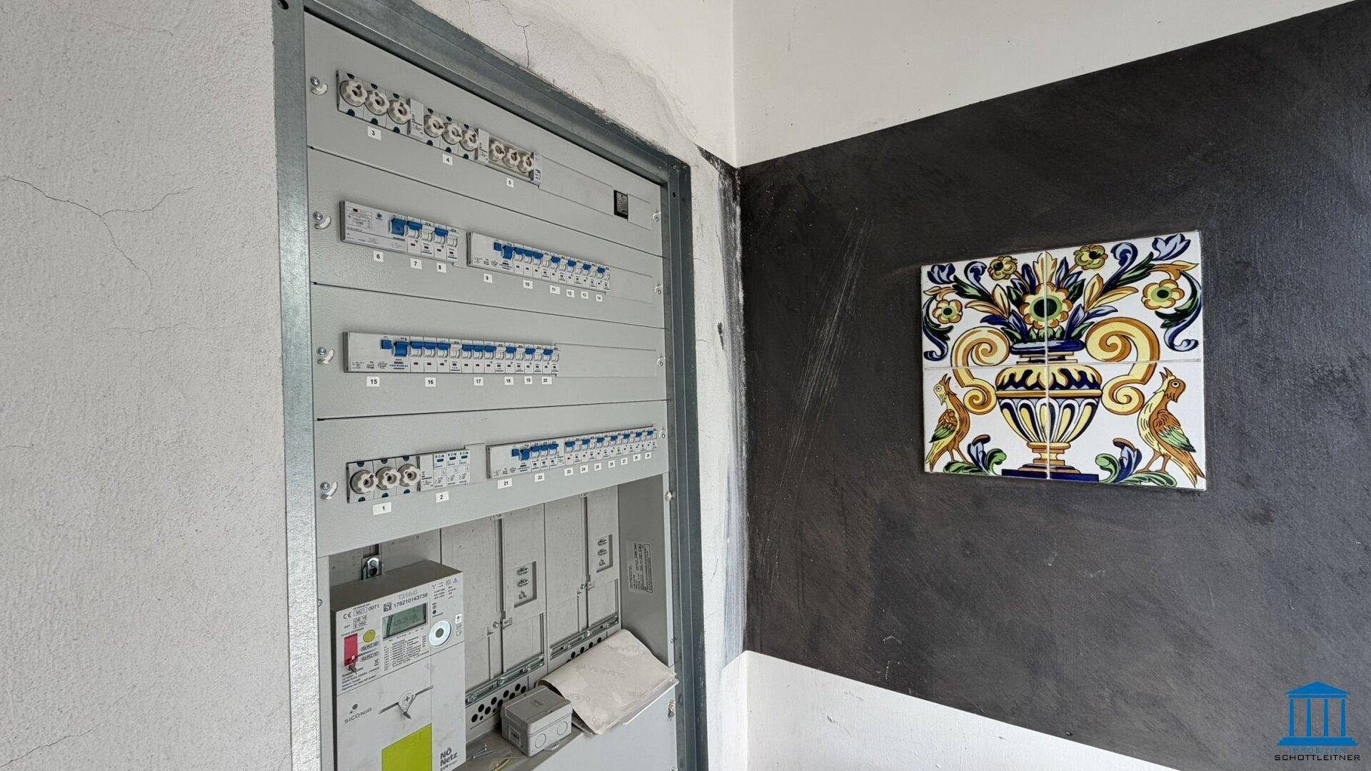 Elektrischer Sicherungskasten an einer Wand mit dunkler Akzentfarbe und dekorativer Fliese.