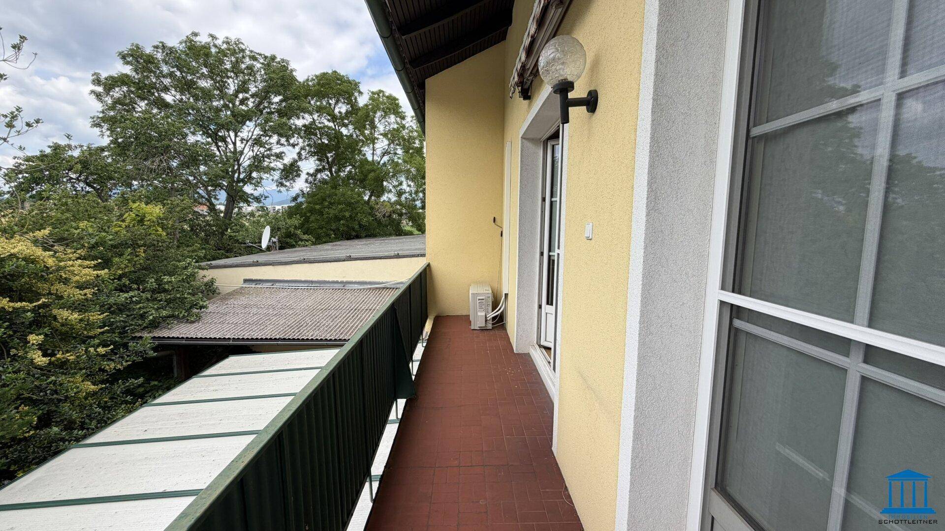 Balkon mit Fliesenboden und Blick auf die Umgebung, inklusive Klimaanlage an der Wand.