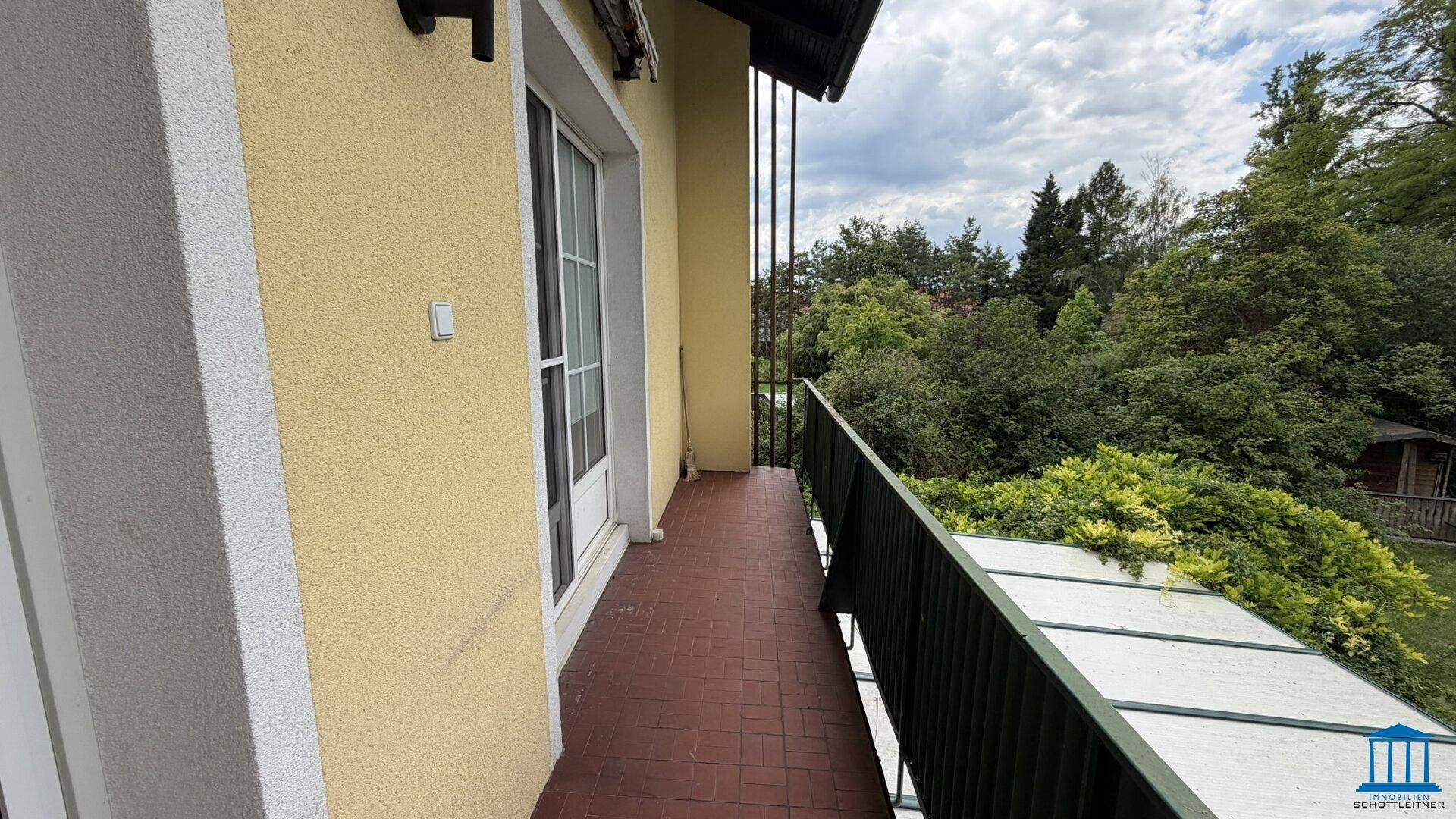 Schmaler Balkon mit Fliesenboden und Metallgeländer, bietet einen Blick ins Grüne.