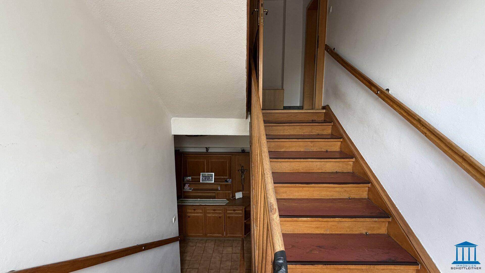 Holztreppe mit Geländer, die in das obere Stockwerk führt, mit Blick auf den Eingangsbereich.