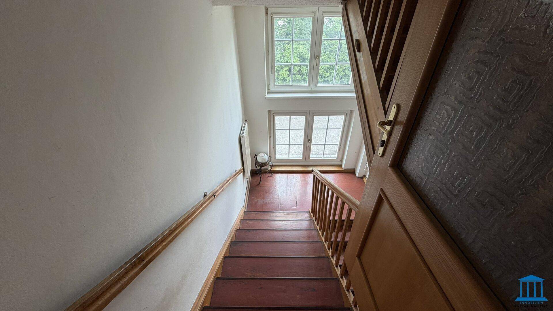 Treppenaufgang mit Holzstufen und Fenstern, die viel Licht hereinlassen.