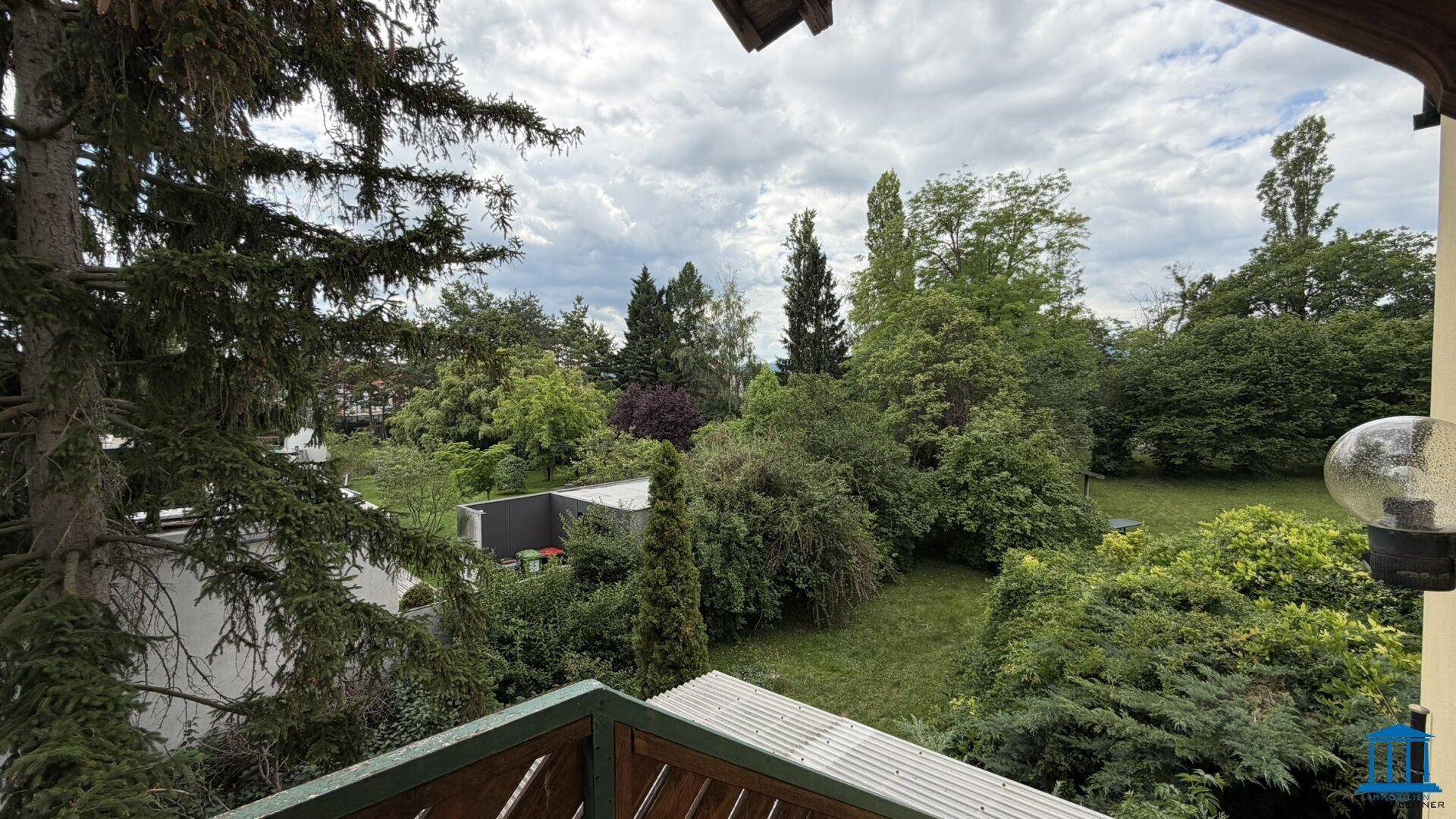 Balkon mit Blick auf die grüne Umgebung und die Dächer der Nachbarhäuser.
