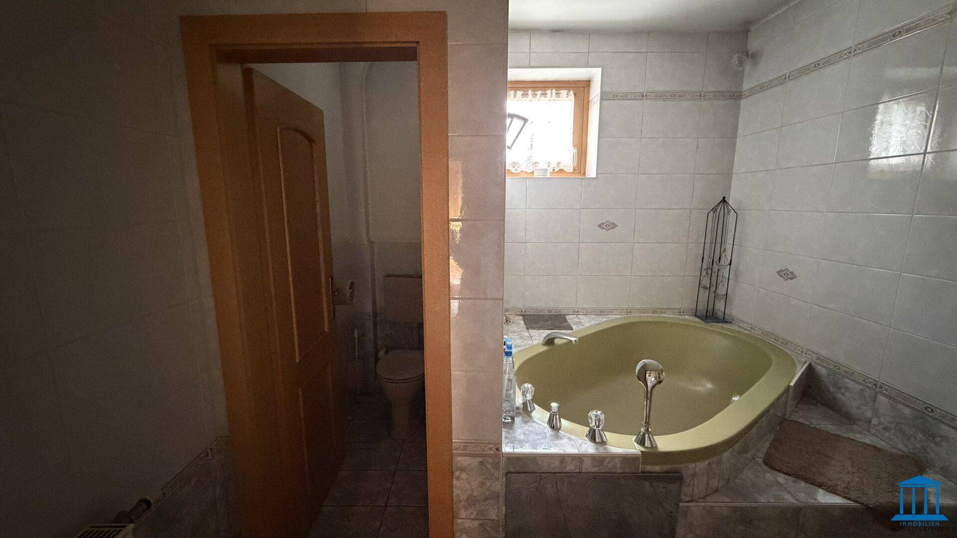 Badezimmer mit gelber Badewanne und Zugang zu einer separaten Toilette, funktional und gut beleuchtet.