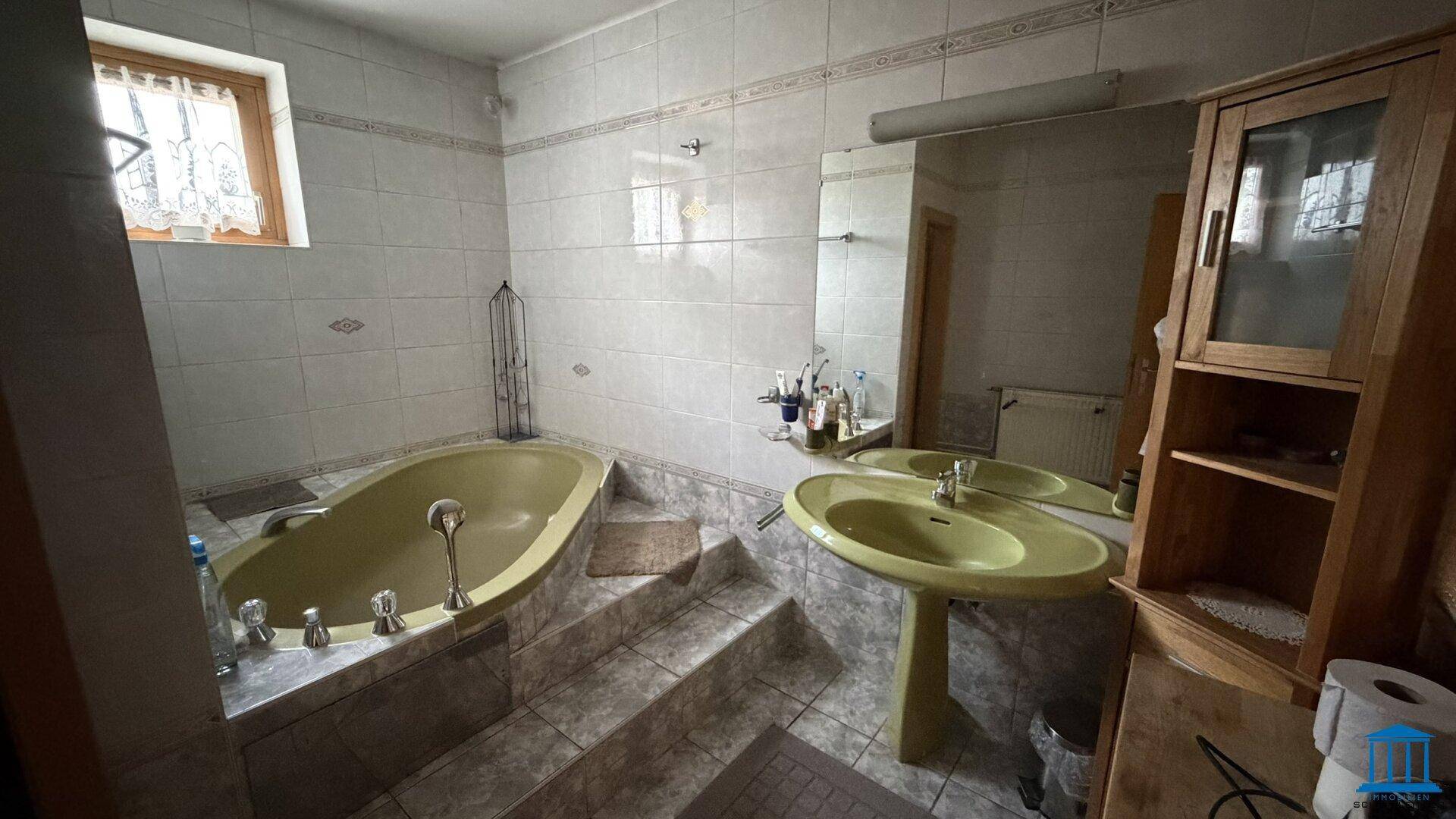 Badezimmer mit gelber Badewanne und Waschbecken, weißen Fliesen und Fenster, bietet eine helle und geräumige Umgebung.