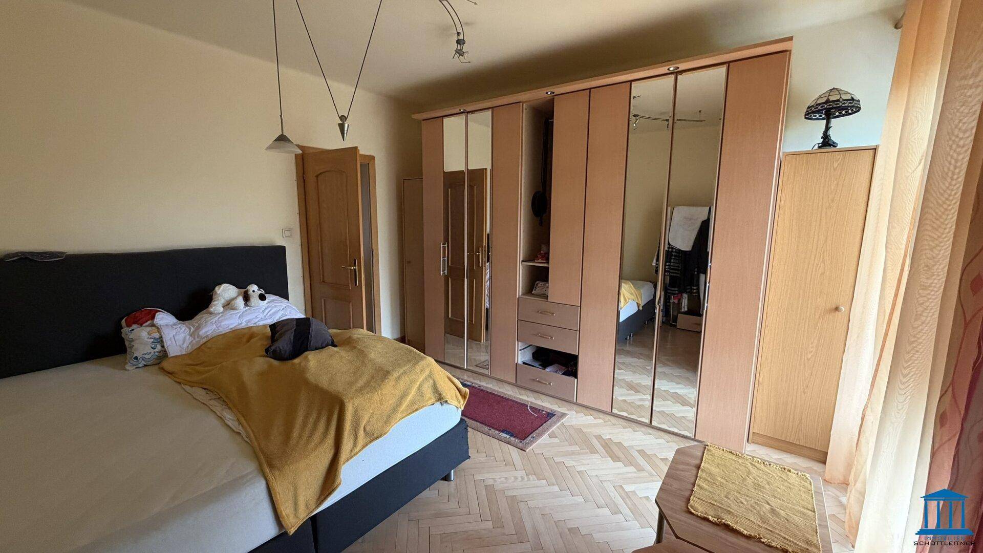 Schlafzimmer mit Doppelbett, großem Spiegelschrank und Holzboden, bietet viel Stauraum und Helligkeit.