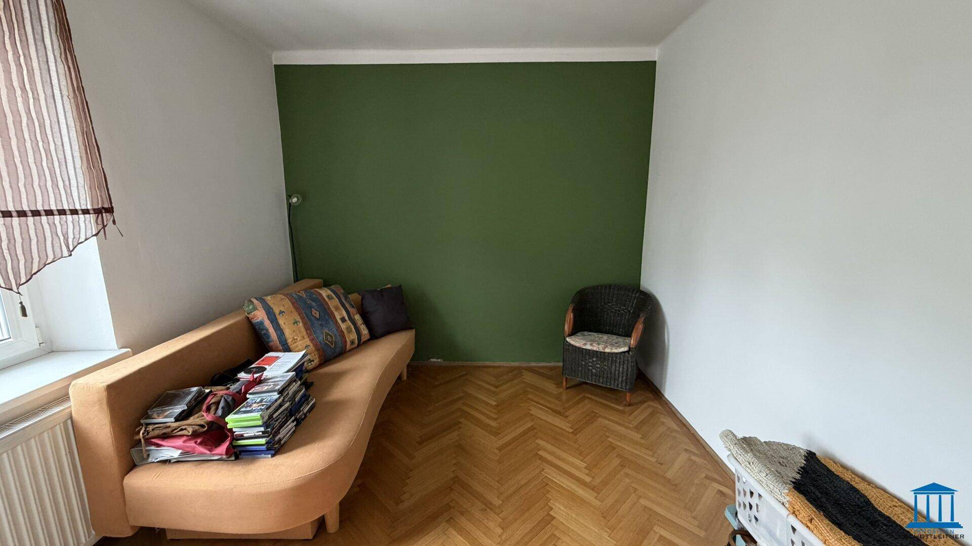 Wohnzimmer mit orangefarbenem Sofa und grüner Akzentwand, Holzboden, schafft eine lebendige Atmosphäre.