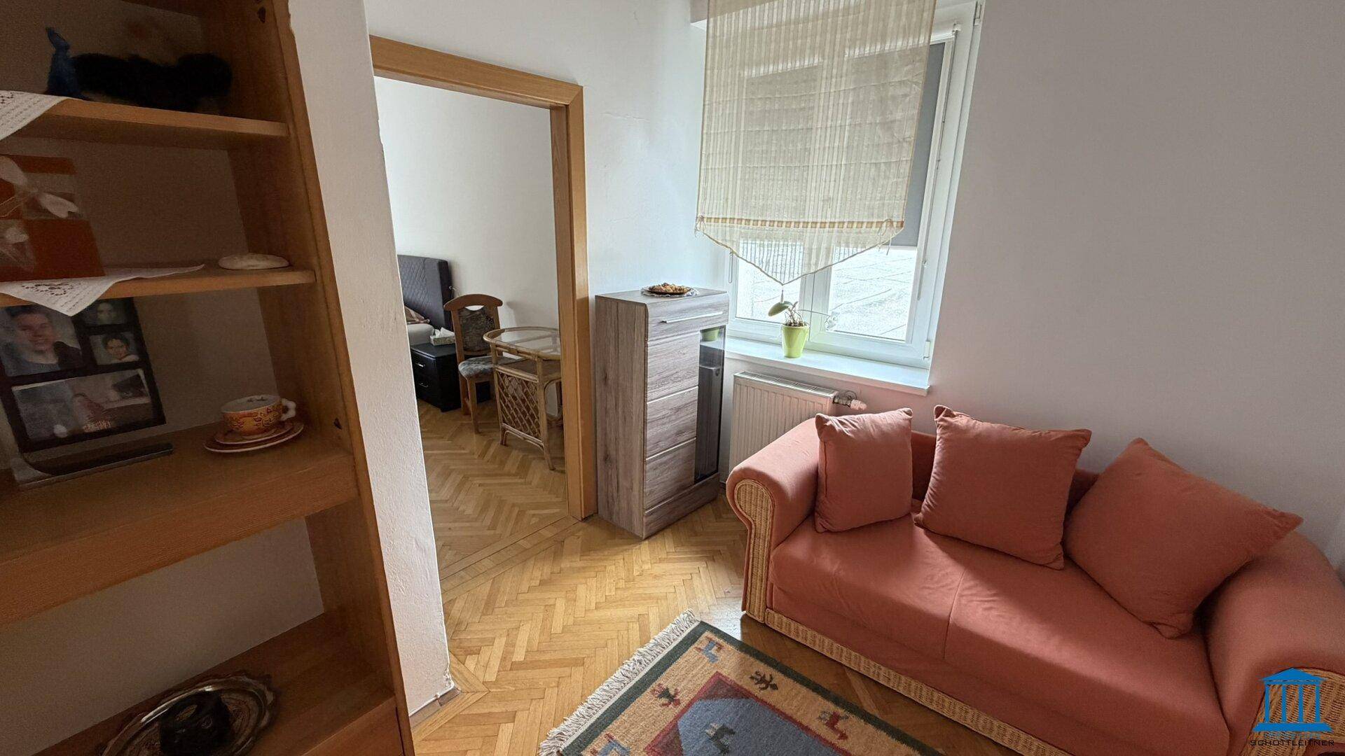Wohnzimmer mit orangefarbenem Sofa und Holzboden, Blick in einen angrenzenden Raum, gemütlich und hell.