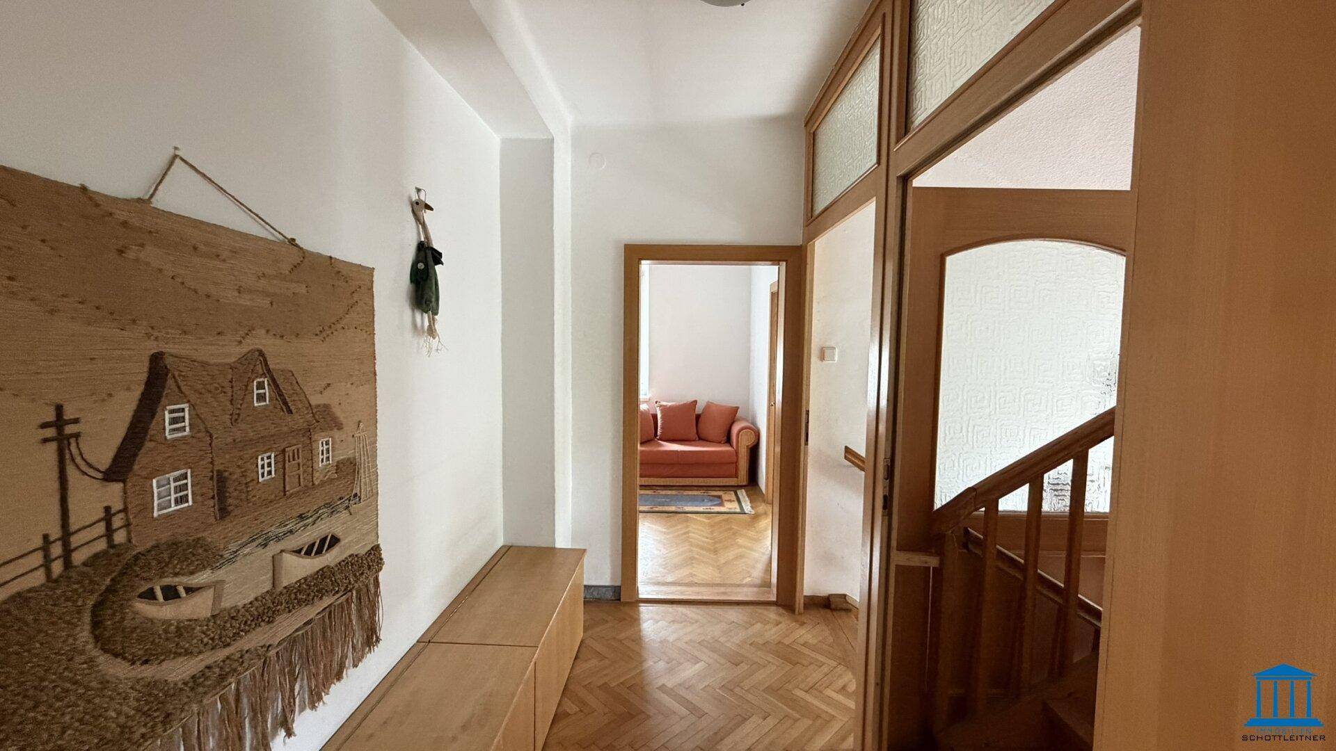 Heller Flur mit Holzboden, Treppenaufgang und Wandteppich, Zugang zu weiteren Räumen, einladend gestaltet.
