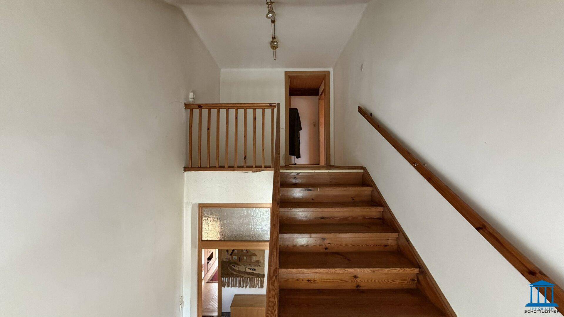 Holztreppe mit Geländer führt nach oben, heller Flur mit Holzboden, verbindet die Wohnebenen.