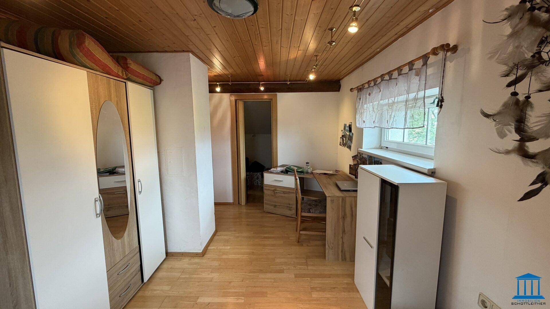 Schlafzimmer im Dachgeschoss mit Holzdecke, Kleiderschrank und Schreibtisch, bietet eine gemütliche Rückzugsmöglichkeit.