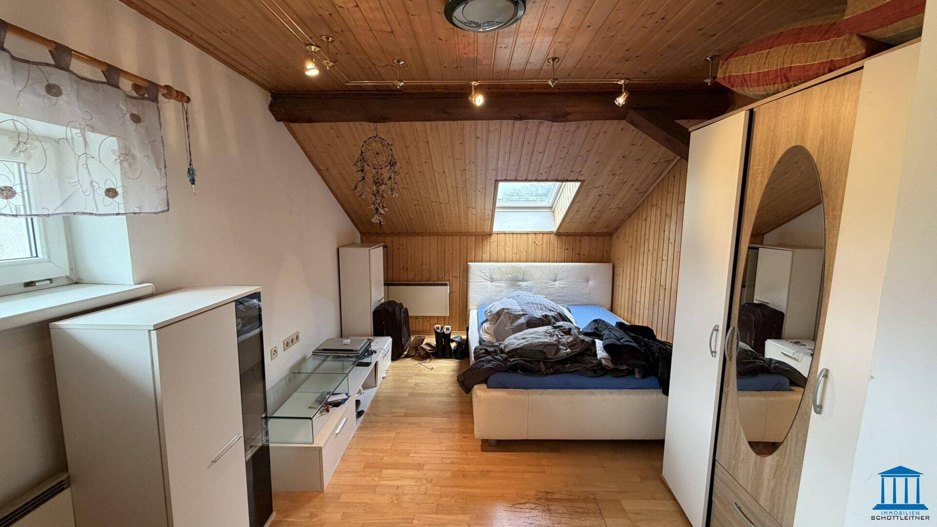 Gemütliches Schlafzimmer im Dachgeschoss mit Holzbalkendecke, Dachfenster und hellen Möbeln.