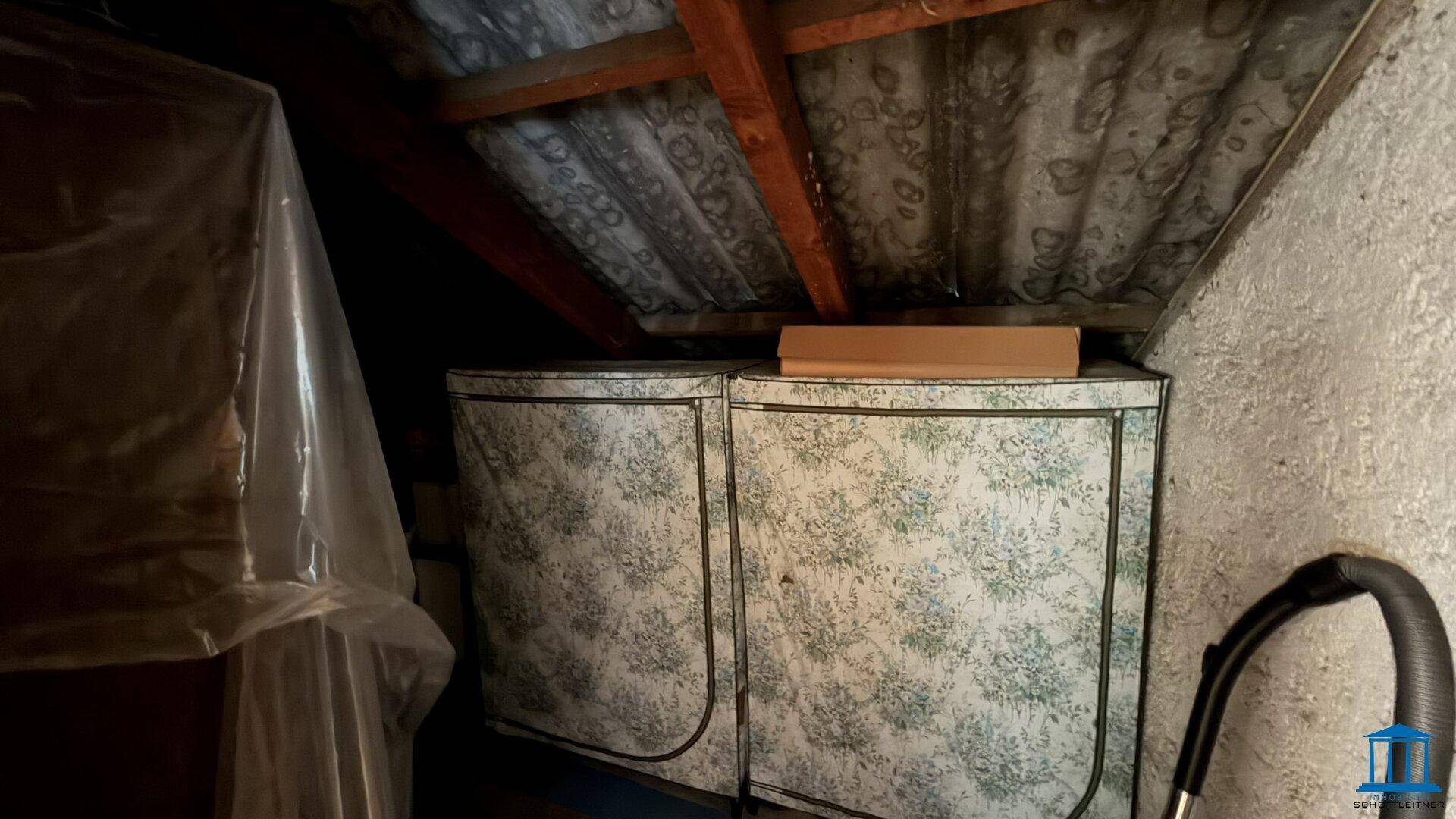 Dachboden-Abstellraum mit schräger Decke, gelagerten Gegenständen und einem Staubsauger.