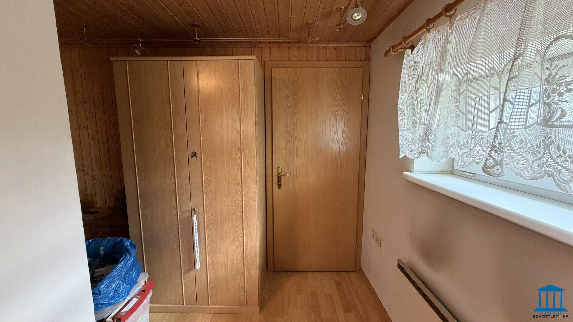 Ecke eines Zimmers mit Holzschrank, Holztür und einem Fenster mit traditionellem Spitzenvorhang.