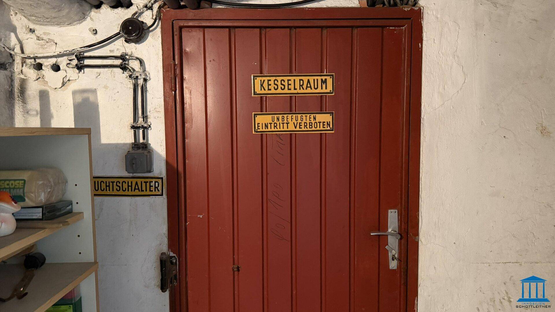 Rote Metalltür in einem Kellerraum, beschriftet als Kesselraum mit Zutrittsverbot.