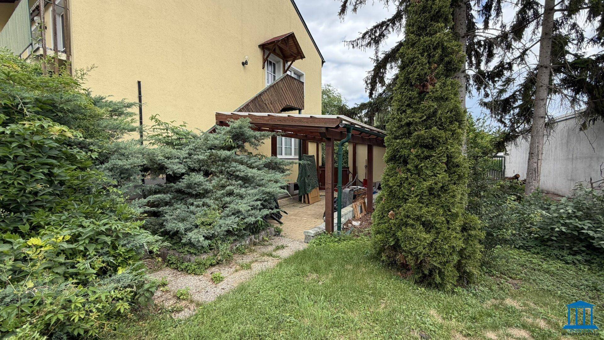Gartenbereich mit überdachter Terrasse und viel Grün, angrenzend an das Gebäude, ideal für Entspannung im Freien.