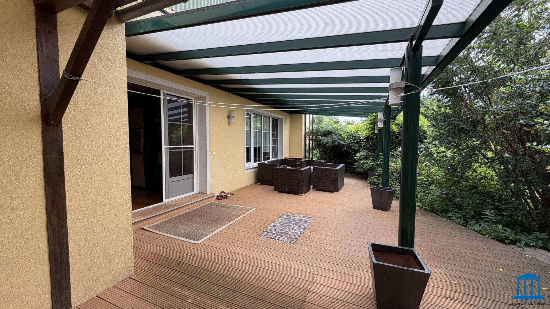 Geräumige, überdachte Holzterrasse mit Blick auf den Garten und viel Grün.