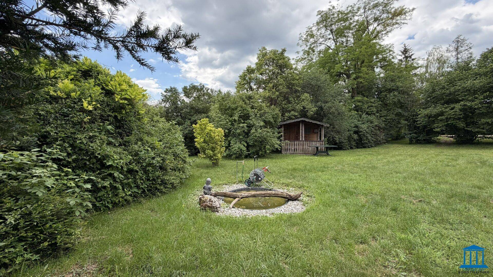 Großer Garten mit Rasenfläche, Teich und einem kleinen Holzhaus im Hintergrund.