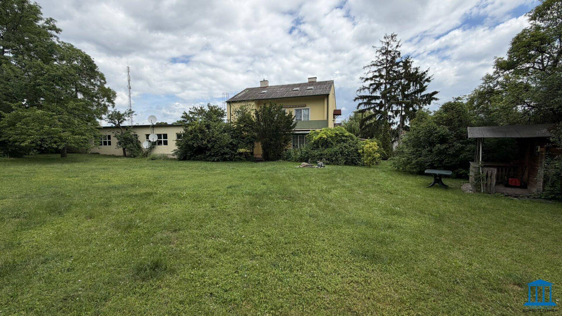 Ansicht des Hauses von der großen Gartenfläche aus, umgeben von viel Grün.