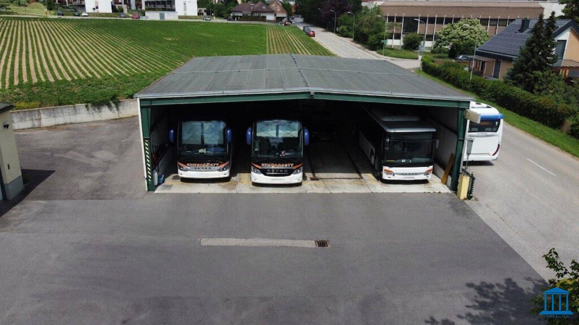 Offene Halle mit mehreren Reisebussen, umgeben von einem Weinberg und einer Straße.