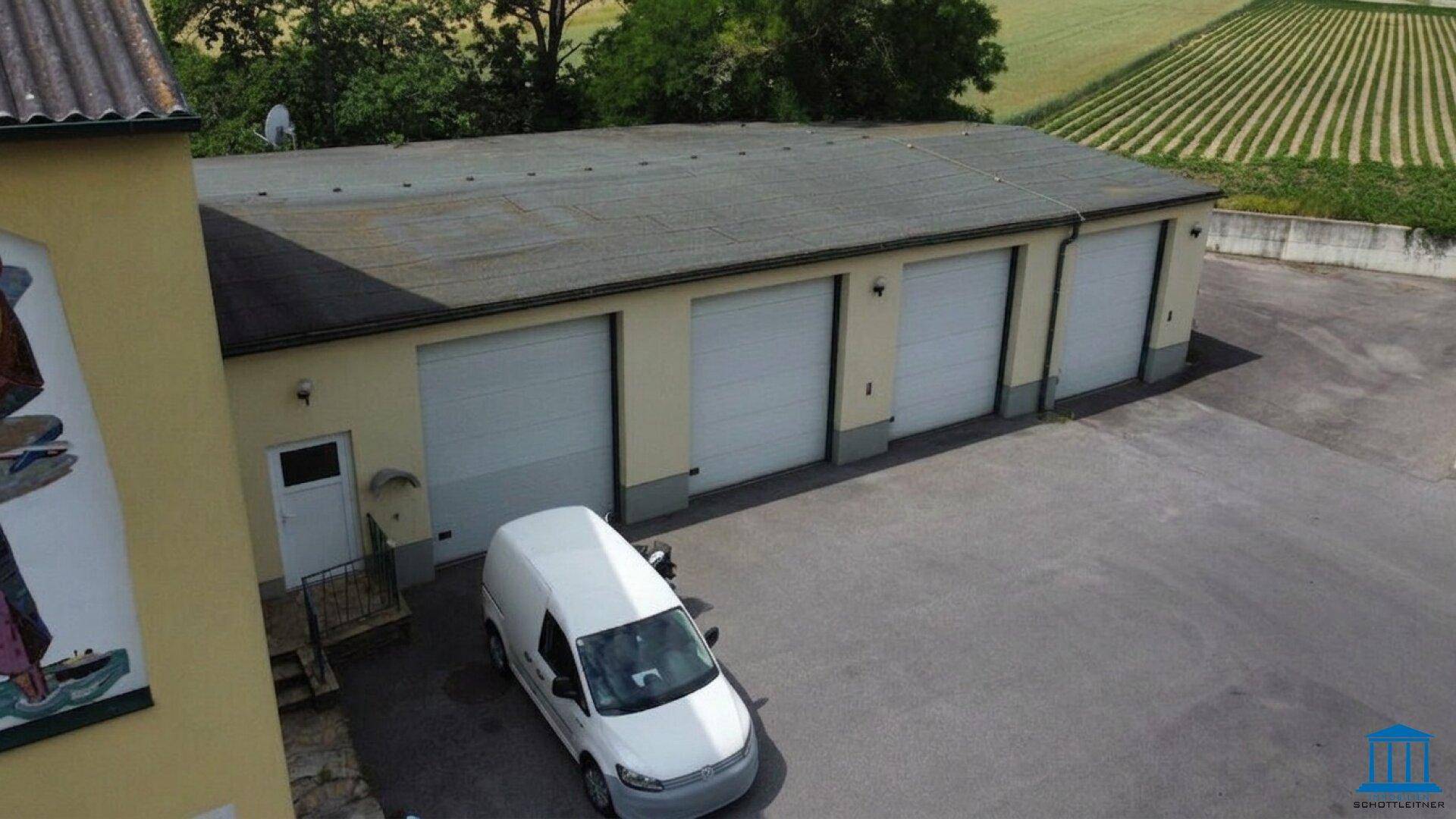 Nahaufnahme der Garagen mit mehreren Rolltoren und einem Lieferwagen davor, angrenzend an das Hauptgebäude.